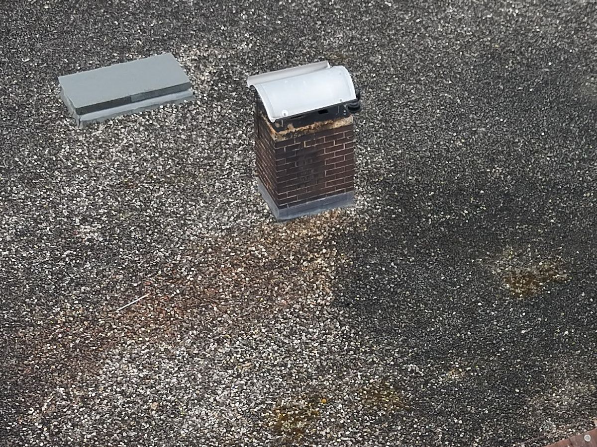 Gemauerter Schornsteinkopf mit Blechhaube auf einem Flachdach